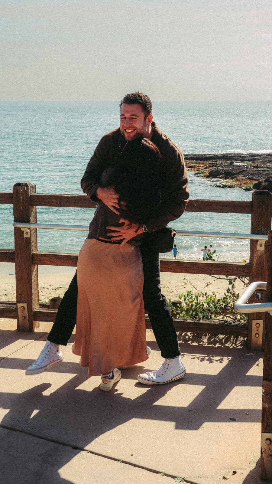 man laughing as he lifts a woman off her feet in a hug at a beach overlook