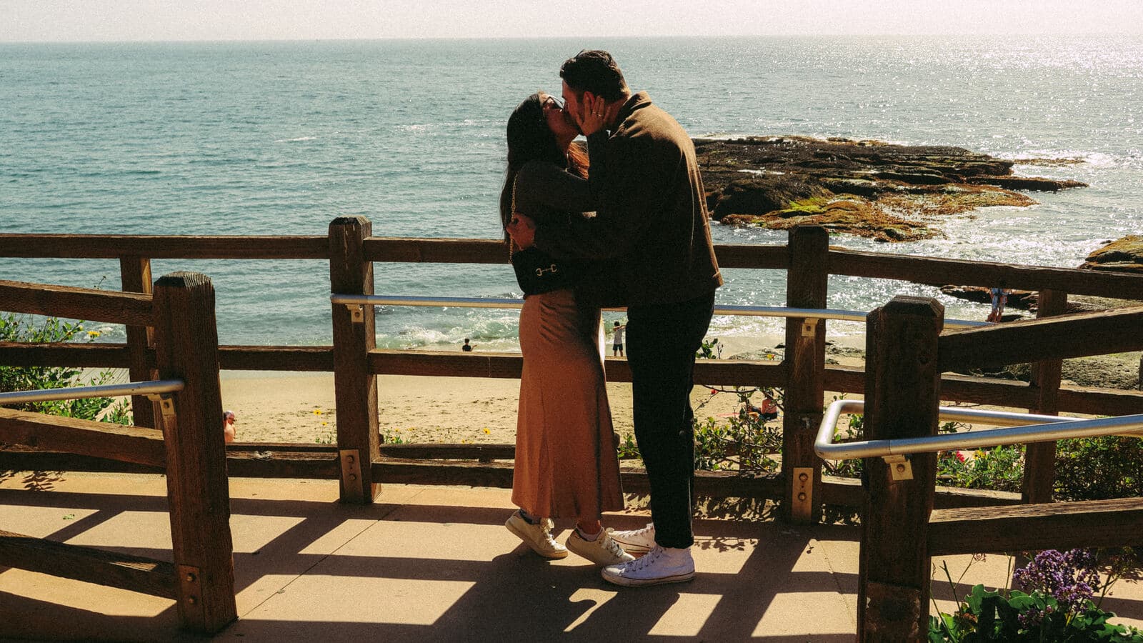 couple kissing in an embrace at a beachside boardwalk railing