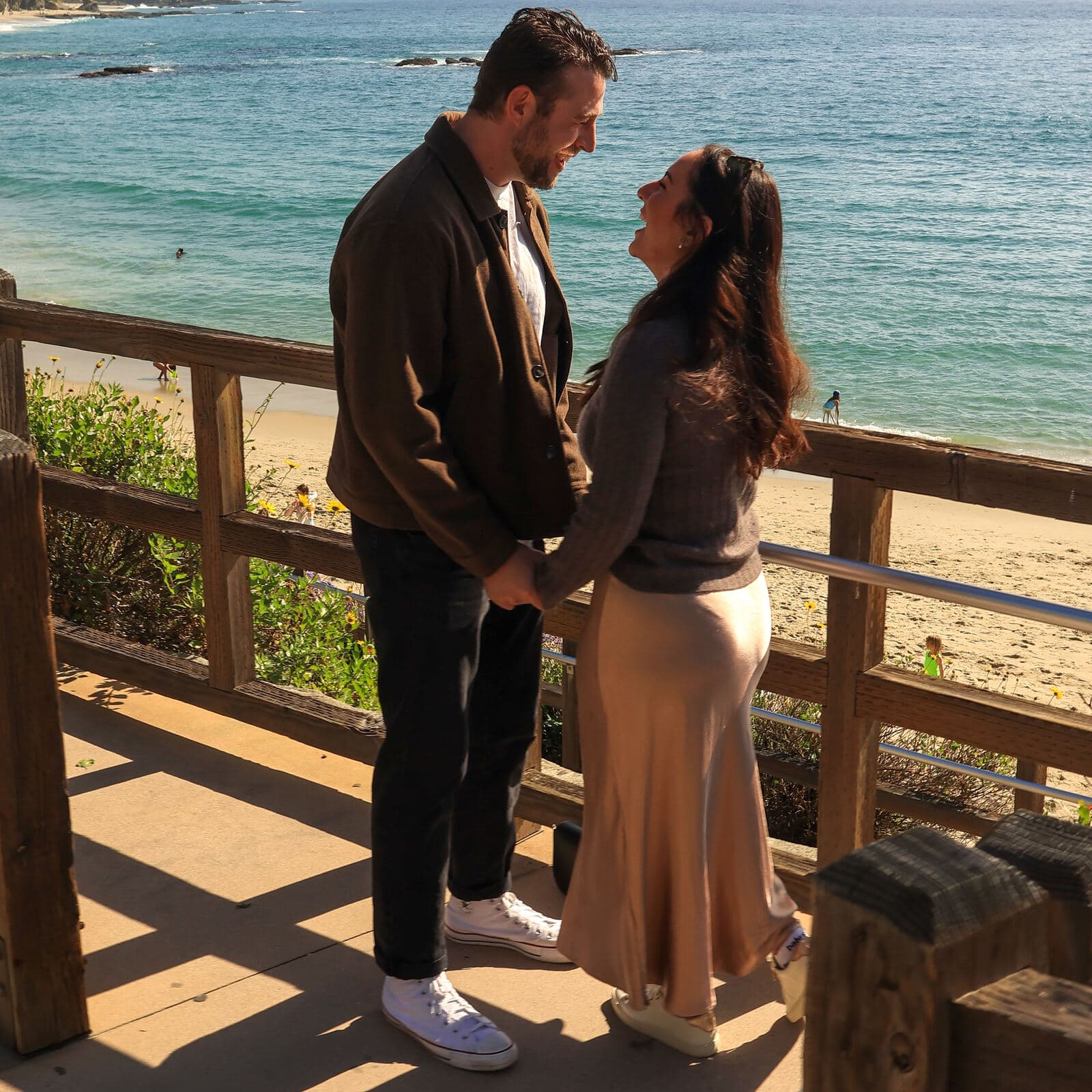 couple holding hands and gazing at each other at a wooden overlook above a bright blue cove