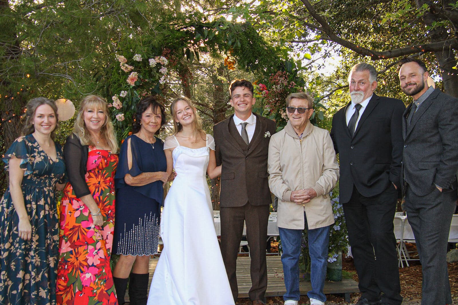 bride and groom lined up with family members in front of a garden ceremony arch