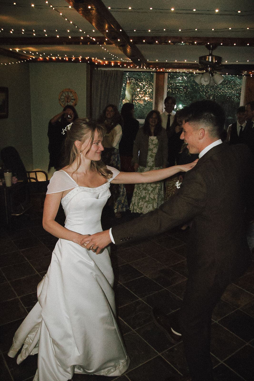 bride and groom sharing their first dance under string lights as guests watch
