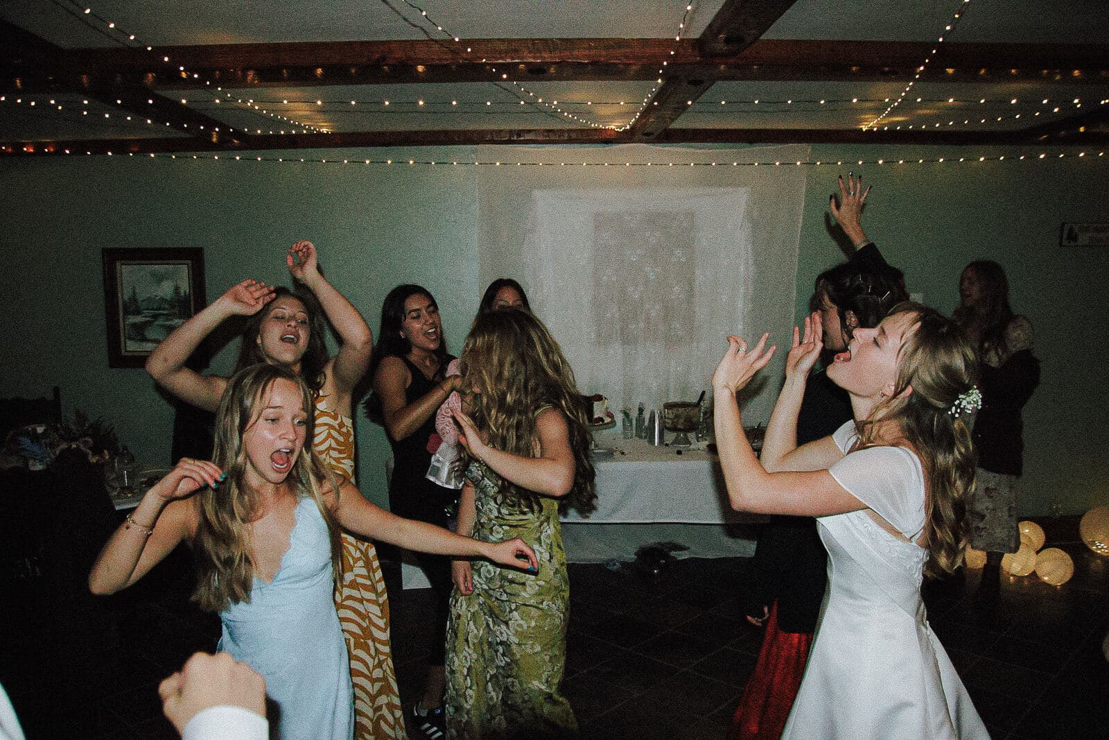 bride singing and dancing with a crowd of guests under string lights