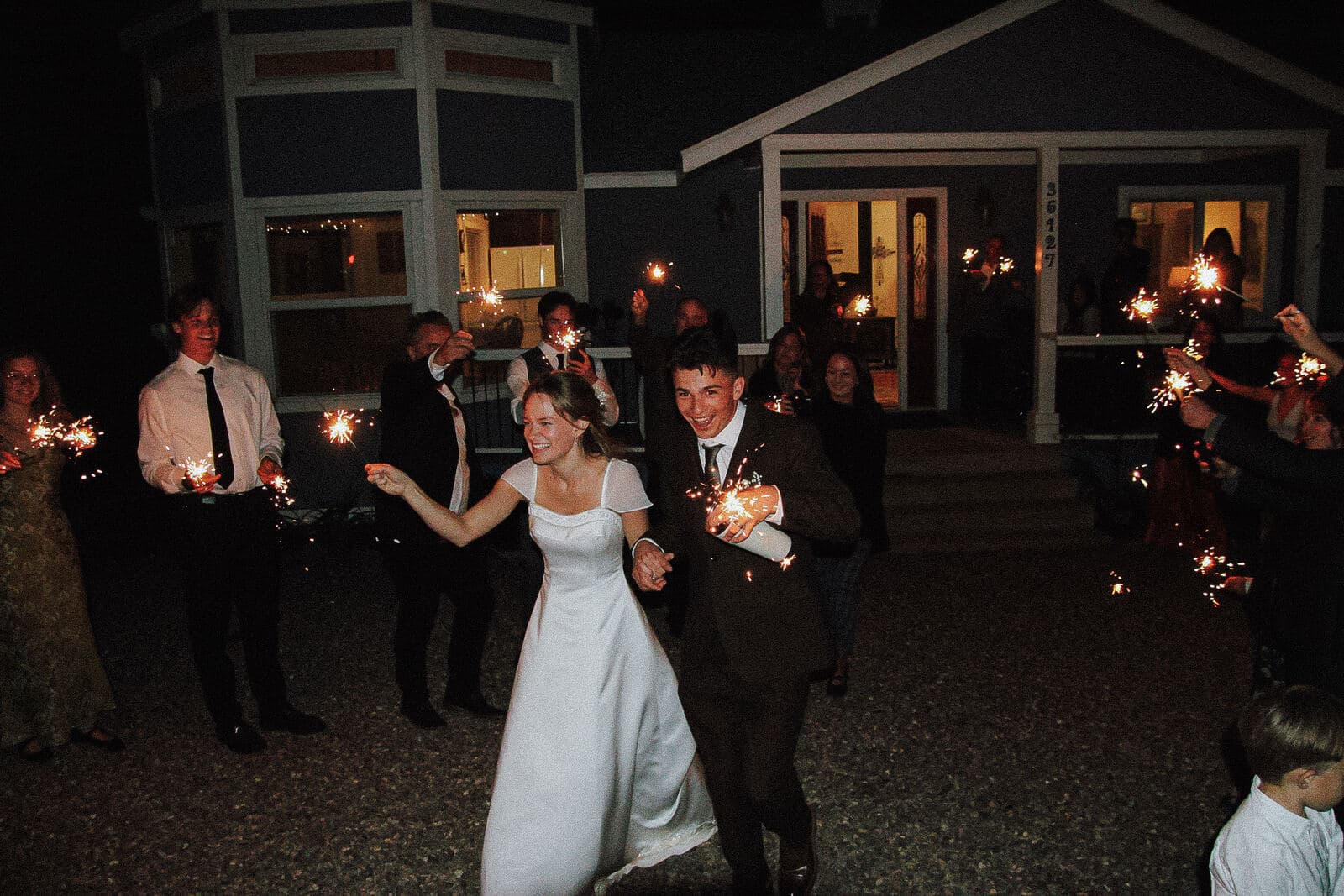 bride and groom laughing as they run through a tunnel of sparklers at night